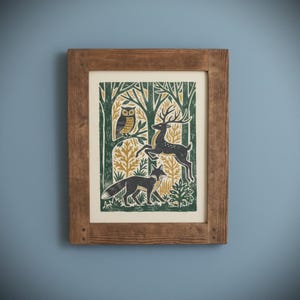 May include: A framed art print featuring a forest scene with an owl, deer, and fox. The print has a green, gold, and black color scheme. The frame is made of wood and has a natural finish. The artwork is mounted on a cream-colored background.