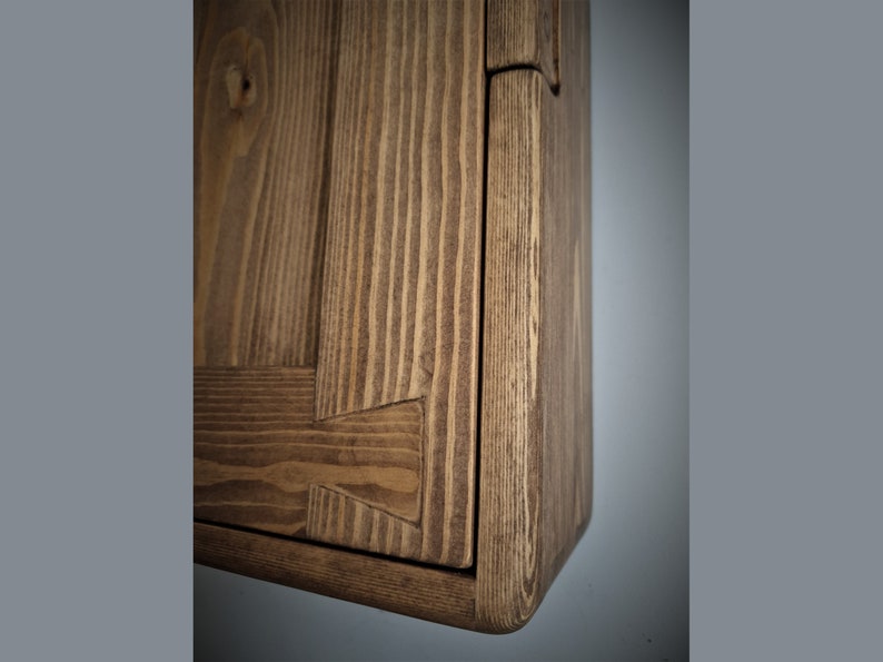 Puede incluir: Primer plano de una esquina de un armario de madera con un acabado marr&oacute;n natural. El armario tiene un dise&ntilde;o sencillo con un borde biselado y un patr&oacute;n de veta visible.