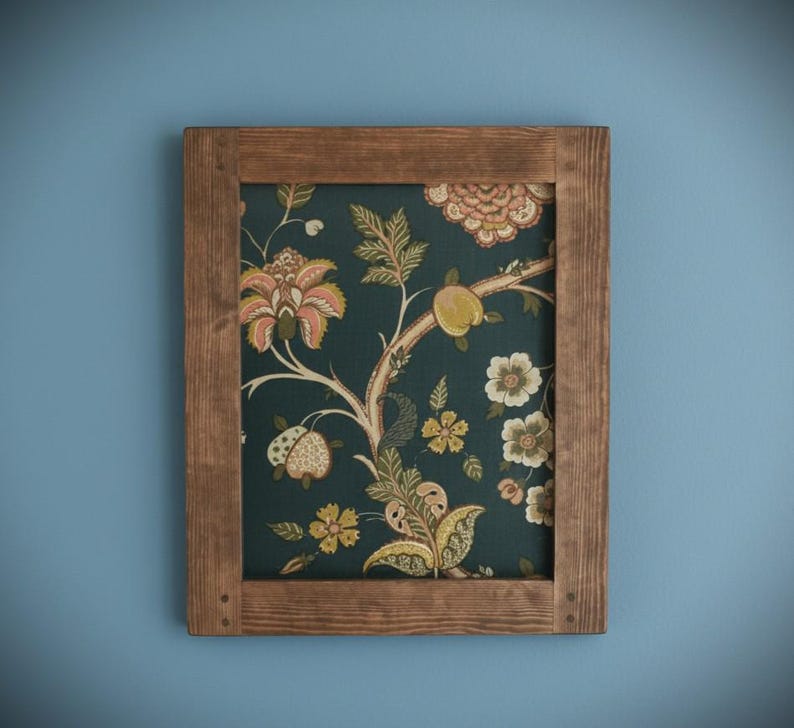 May include: A framed floral print with a dark teal background and a brown wooden frame. The print features a botanical design with peach, yellow, and white flowers and fruit. The frame is made of natural wood.