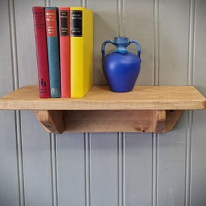 May include: A wooden shelf with a blue ceramic vase and four books. The books are titled "Gone With The Wind", "The Big Sleep", "Seal In The Morning", and "Sunday Creatures".
