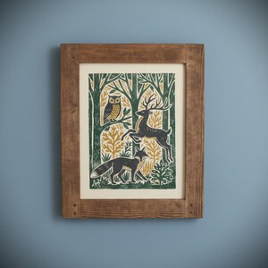 May include: A framed art print featuring a forest scene with an owl, deer, and fox. The print has a green, gold, and black color scheme. The frame is made of wood and has a natural finish. The artwork is mounted on a cream-colored background.
