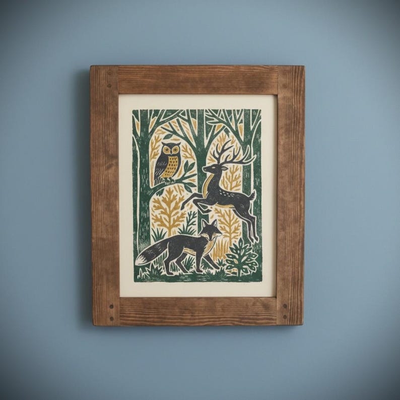 May include: A framed art print featuring a forest scene with an owl, deer, and fox. The print has a green, gold, and black color scheme. The frame is made of wood and has a natural finish. The artwork is mounted on a cream-colored background.
