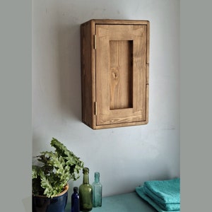 Puede incluir: Un armario de pared de madera r&uacute;stica con una sola puerta. El armario est&aacute; hecho de madera natural con un acabado marr&oacute;n claro. La puerta tiene un dise&ntilde;o sencillo con un marco rectangular y una peque&ntilde;a manija.