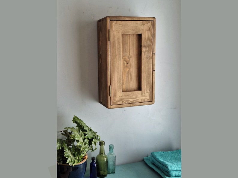 Puede incluir: Un armario de pared de madera r&uacute;stica con una sola puerta. El armario est&aacute; hecho de madera natural con un acabado marr&oacute;n claro. La puerta tiene un dise&ntilde;o sencillo con un marco rectangular y una peque&ntilde;a manija.