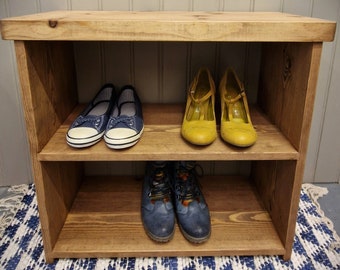 May include: A two-tier wooden shoe rack with a natural wood grain finish. The top shelf holds a pair of blue canvas trainers and a pair of yellow t-strap heels. The bottom shelf holds a pair of blue leather lace-up boots.