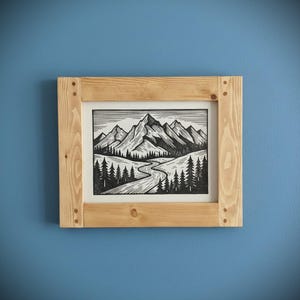 May include: A framed black and white mountain landscape art print. The artwork depicts a winding river, trees, and towering mountains. The print is set in a natural wood frame with visible wood grain and corner joints, mounted on a blue wall.