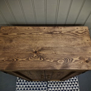 May include: A rectangular wooden cabinet top with a dark brown stained finish, showcasing prominent wood grain patterns, knots, and small circular metal nail heads embedded along the edges of the flat surface.