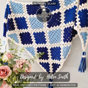 Puede incluir: Un chal de zafiro tejido a mano con un patrón geométrico en tonos azules y crema. El chal tiene forma triangular y está adornado con borlas. El texto "Sapphire Scarf", "PDF Pattern", "Designed by Helen Smith", "Real Crochet Pattern" y "Not AI Generated" son visibles.