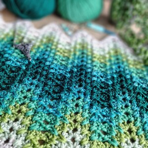 May include: A handmade crochet project in shades of green, teal, and white. The textured fabric is in a chevron pattern. The image also shows balls of green yarn and a crochet hook, suggesting a crafting theme.