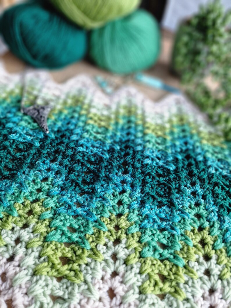 May include: A handmade crochet project in shades of green, teal, and white. The textured fabric is in a chevron pattern. The image also shows balls of green yarn and a crochet hook, suggesting a crafting theme.