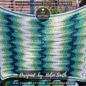 May include: A handmade crochet blanket with a chevron pattern in shades of white, teal, and green. The blanket has a scalloped edge and is adorned with tassels at each corner. Text on the blanket reads "WALKING THROUGH THE FOREST BLANKET" and "Designed by Helen Smith".