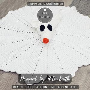 May include: A white crocheted puppy comforter with a round, scalloped edge. The puppy's head has black eyes, an orange nose, and white ears. Text on the image reads "PUPPY ZERO COMFORTER", "PDF PATTERN", "Designed by Helen Smith", and "REAL CROCHET PATTERN • NOT AI GENERATED".