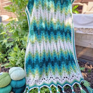 May include: A handmade crochet shawl in shades of teal, green, and white, with a chevron pattern. The shawl has a scalloped edge with teal and white tassels. Several balls of yarn in matching colors are visible.