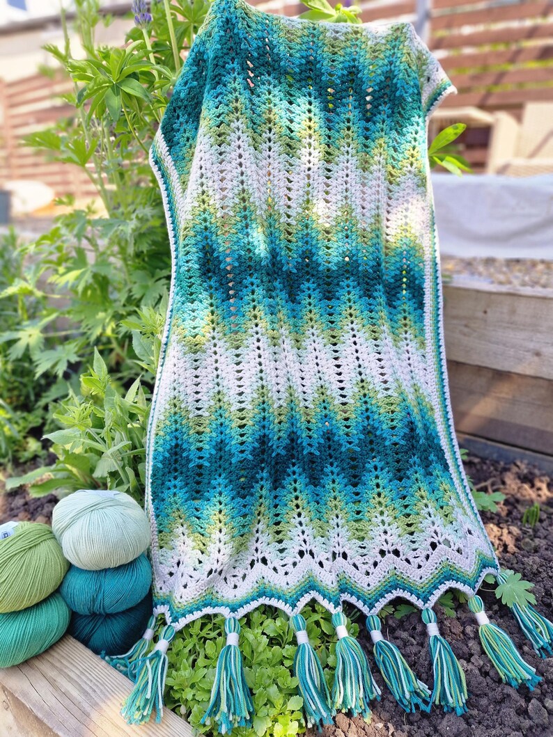 May include: A handmade crochet shawl in shades of teal, green, and white, with a chevron pattern. The shawl has a scalloped edge with teal and white tassels. Several balls of yarn in matching colors are visible.