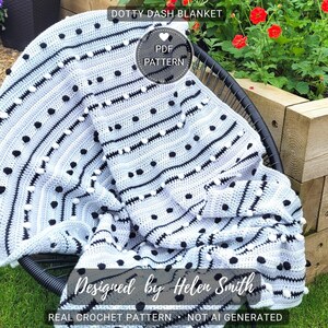 Może przedstawiać: Ręcznie robiony, jasnoszary koc z czarnymi kropkami i paskami, narzucony na czarny fotel. Na kocu widnieje napis "DOTTY DASH BLANKET" oraz "Designed by Helen Smith". Widoczne są również słowa "REAL CROCHET PATTERN NOT AI GENERATED".