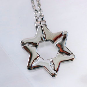 Peut inclure: Un collier en chaîne argent avec un pendentif en forme d'étoile à six branches en argent. L'étoile est composée de deux pièces qui s'emboîtent.