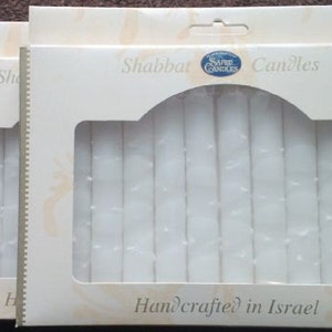 Puede incluir: Dos paquetes de velas de Shabat blancas, cada uno con una ventana de pl&aacute;stico transparente que muestra las velas en el interior. Los paquetes est&aacute;n etiquetados como "Shabbat Candles" y "Handcrafted in Israel".