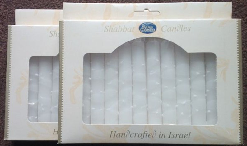 Puede incluir: Dos paquetes de velas de Shabat blancas, cada uno con una ventana de pl&aacute;stico transparente que muestra las velas en el interior. Los paquetes est&aacute;n etiquetados como "Shabbat Candles" y "Handcrafted in Israel".