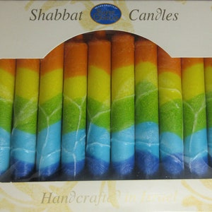 Puede incluir: Una caja de velas de Shabat de colores arco&iacute;ris. Las velas est&aacute;n hechas a mano y tienen un esquema de colores azul, verde, amarillo y naranja. La caja dice "Shabbat Candles" y "Handcrafted in Israel".