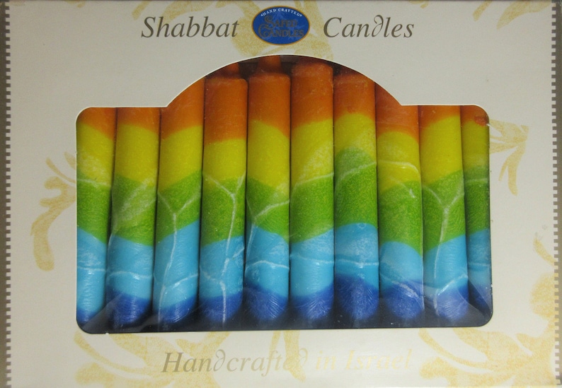 Puede incluir: Una caja de velas de Shabat de colores arco&iacute;ris. Las velas est&aacute;n hechas a mano y tienen un esquema de colores azul, verde, amarillo y naranja. La caja dice "Shabbat Candles" y "Handcrafted in Israel".