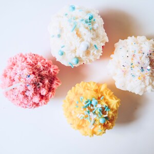May include: Four frosted cupcakes with colorful sprinkles. The cupcakes are pink, white, yellow, and white.