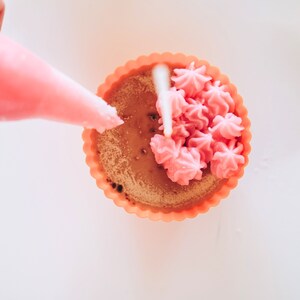 May include: A pink cupcake with a swirl of pink frosting in a light orange cupcake liner.
