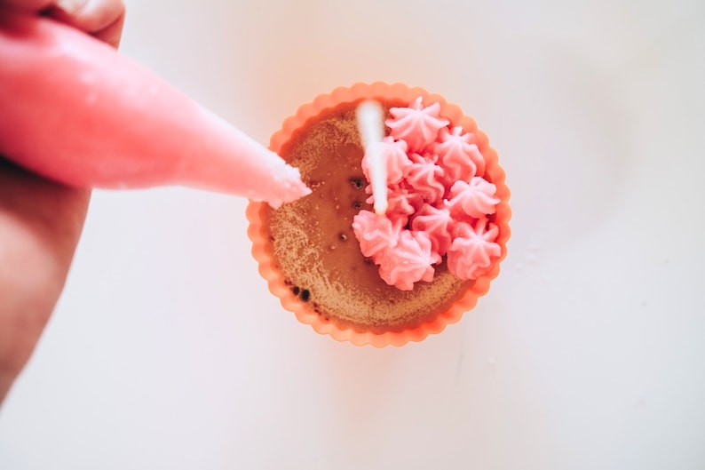 May include: A pink cupcake with a swirl of pink frosting in a light orange cupcake liner.