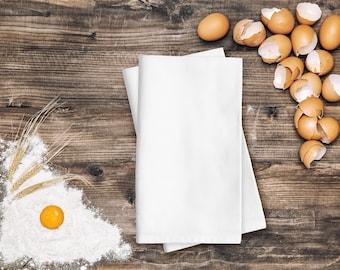 May include: A white kitchen towel folded on a wooden table with a pile of broken eggshells and a bowl of flour with wheat stalks.