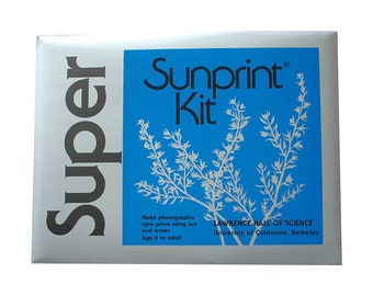 May include: A silver box with the words "Super Sunprint Kit" printed on it. The box has a blue background with a white plant illustration and the text "Make photographic type prints using sun and water. Age 6 to adult. LAWRENCE HALL OF SCIENCE University of California, Berkeley."