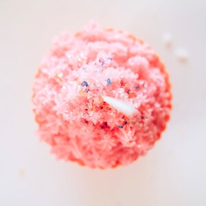 May include: Pink cupcake candle with white frosting and blue and pink sprinkles.
