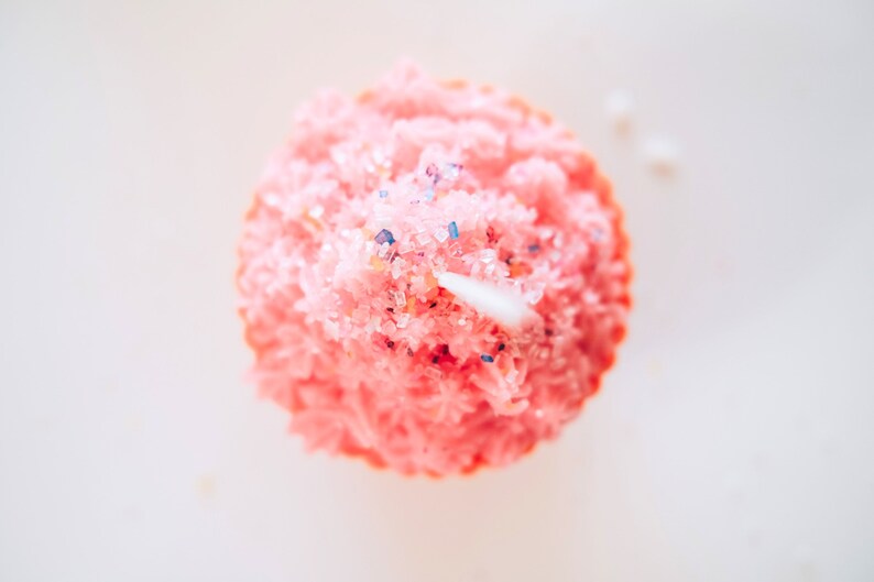 May include: Pink cupcake candle with white frosting and blue and pink sprinkles.