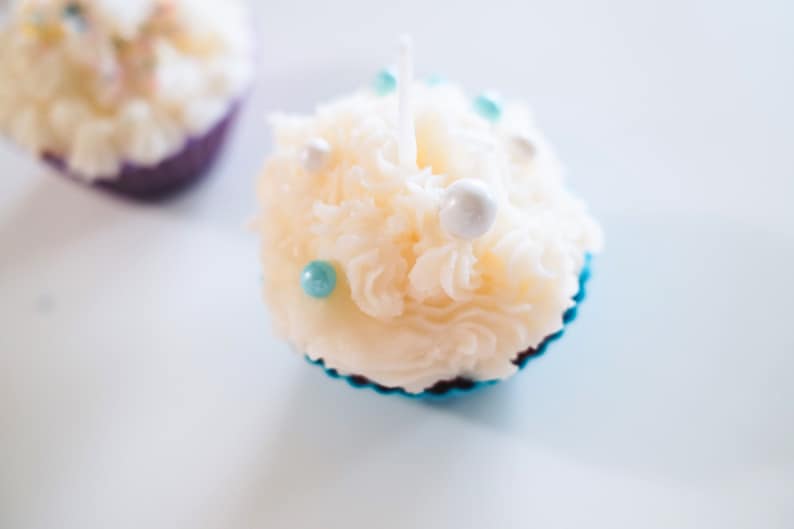 May include: A white cupcake with blue and white sprinkles and a white candle in the center. The cupcake is sitting on a blue cupcake liner.