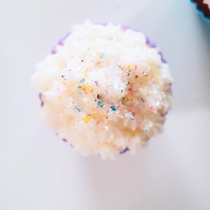 May include: A white cupcake with purple frosting and colorful sprinkles on top.