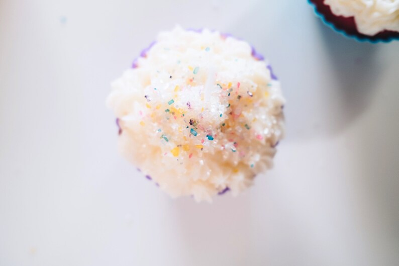 May include: A white cupcake with purple frosting and colorful sprinkles on top.