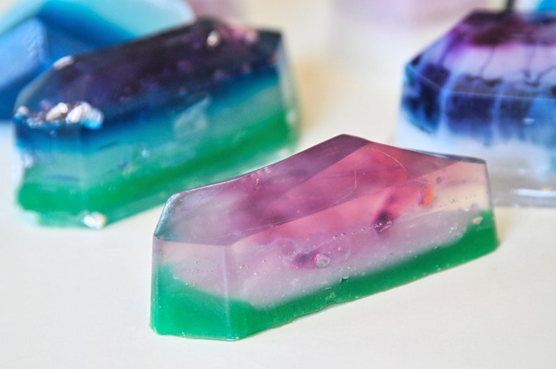 May include: A set of three layered, translucent, geometric soaps in shades of green, blue, purple, and white. The soaps are shaped like crystals and have a glossy finish.