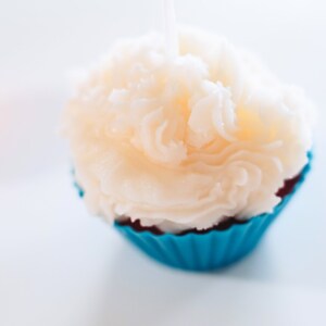 May include: A white cupcake candle with a blue and red cupcake liner. The candle is shaped like a cupcake with white frosting.