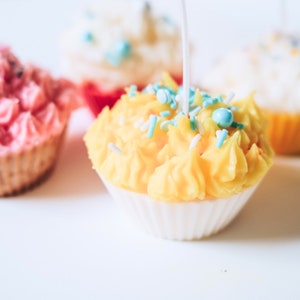 May include: Three cupcake candles with pink, yellow, and white frosting. Each candle has sprinkles and a wick.