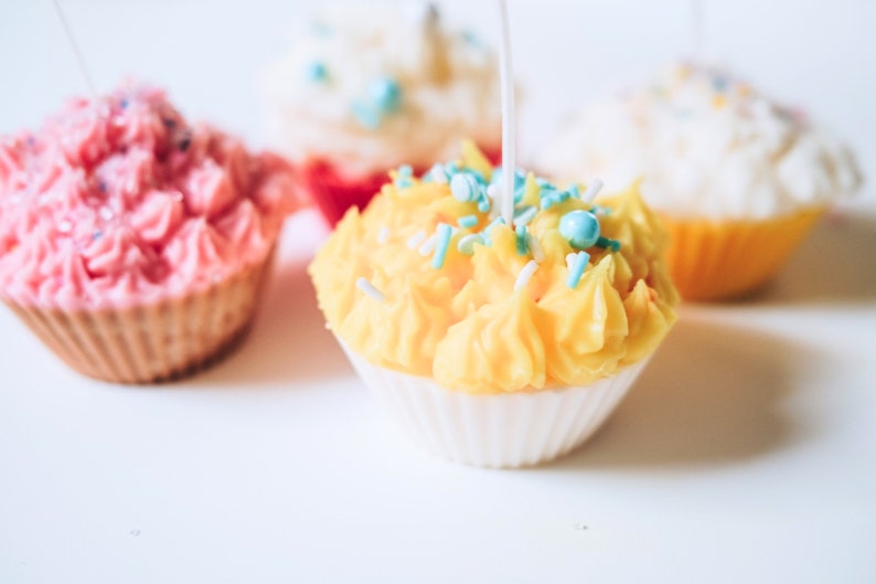 May include: Three cupcake candles with pink, yellow, and white frosting. Each candle has sprinkles and a wick.
