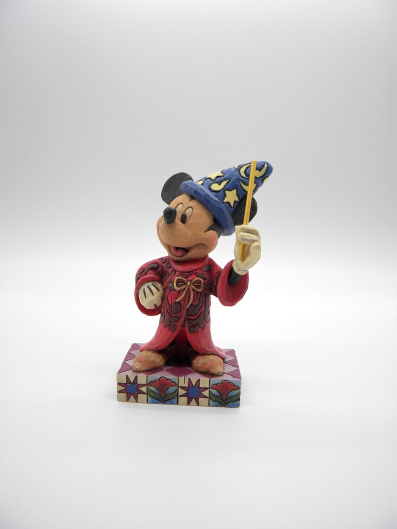 Op de afbeelding: Mickey Mouse-beeldje als tovenaar, met een blauwe hoed met gele sterren en een gele toverstaf. De rode mantel heeft gedetailleerde patronen en het beeldje staat op een decoratieve basis.