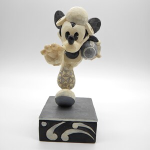 Puede incluir: Una figura tallada de Mickey Mouse con uniforme de b&eacute;isbol, sosteniendo una pelota de b&eacute;isbol. La figura es principalmente crema y negra, con una gorra de b&eacute;isbol y un dise&ntilde;o estampado en la pierna. Se encuentra sobre una base rectangular negra con detalles decorativos blancos.