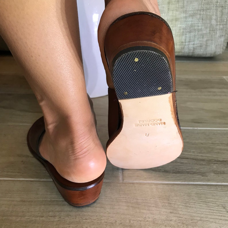 Puede incluir: Sandalias de cuero marr&oacute;n con suela gruesa y banda de rodadura de goma negra. Las sandalias est&aacute;n hechas a mano y tienen el texto "HAND MADE BODRUM" en la suela.