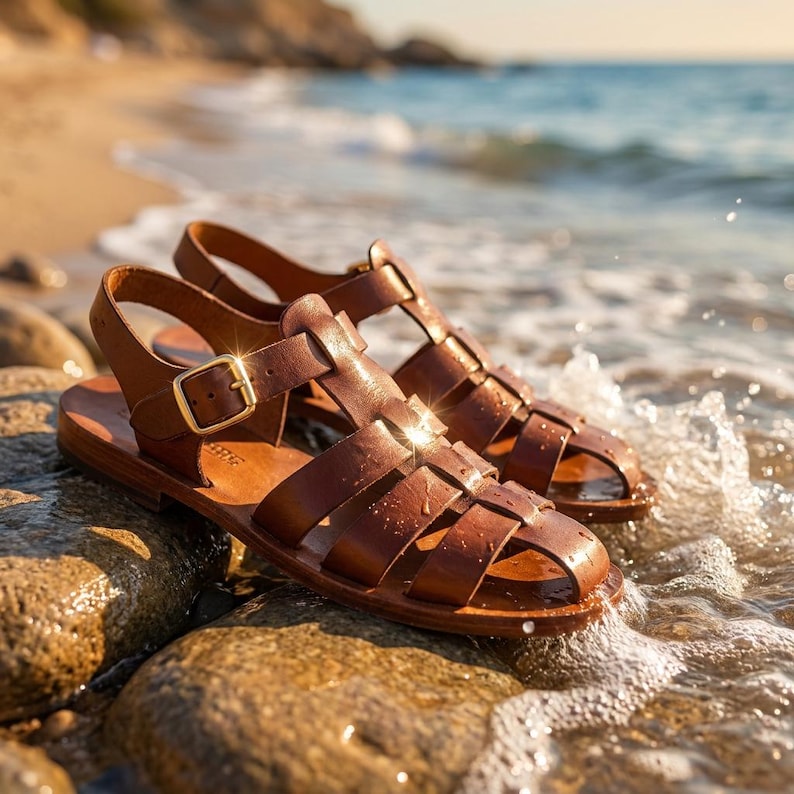 May include: A pair of brown leather sandals with a woven design, featuring a buckle closure and a flat sole. The sandals are resting on wet rocks near the ocean, with the water gently lapping at the edges.