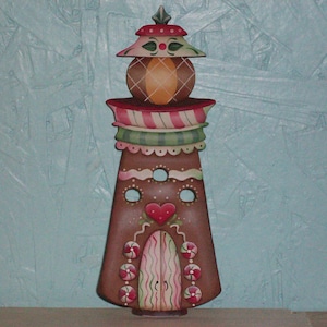 May include: A hand-painted gingerbread house ornament with a candy cane roof, a heart-shaped door, and candy details. The house is brown with white trim and has a green and red striped roof.