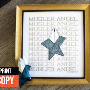 May include: A framed print with the text "MUGLER ANGEL" repeated multiple times. A blue star-shaped bottle of perfume is in the center of the print. The print is in a gold frame.