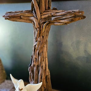 May include: A wooden cross made from driftwood, with a natural brown color. The cross is standing on a wooden base and is surrounded by small white figurines.