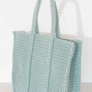May include: A light blue crocheted tote bag with a wide, rectangular shape and two handles.