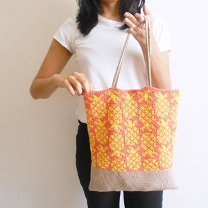 May include: A crocheted tote bag with a geometric pattern in yellow and orange. The bag has a beige bottom and beige straps.