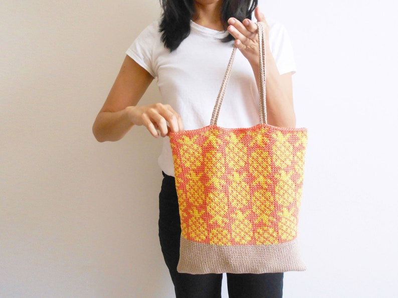 May include: A crocheted tote bag with a geometric pattern in yellow and orange. The bag has a beige bottom and beige straps.