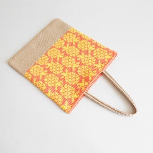 May include: A crocheted tote bag with a yellow and orange pineapple pattern. The bag has a natural jute handle.