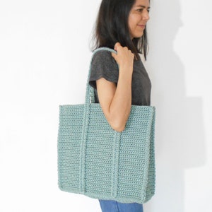 Op de afbeelding: Een lichtblauwe gehaakte tote bag met dikke hengsels. De tas is groot genoeg om dagelijkse benodigdheden te dragen.